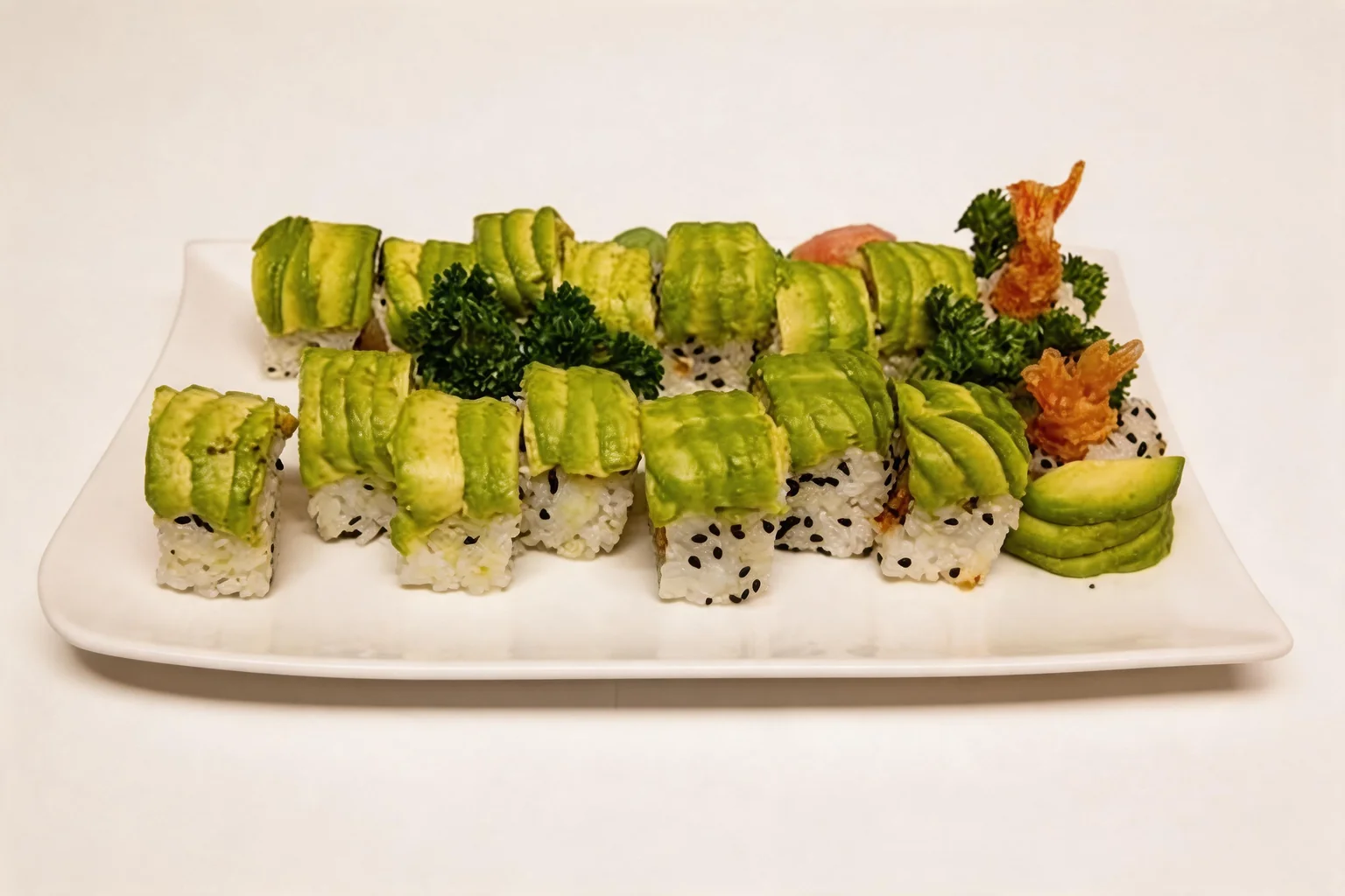 Rouleaux recouverts de fines tranches d'avocat, sur une assiette blanche avec des crevettes tempura en accompagnement