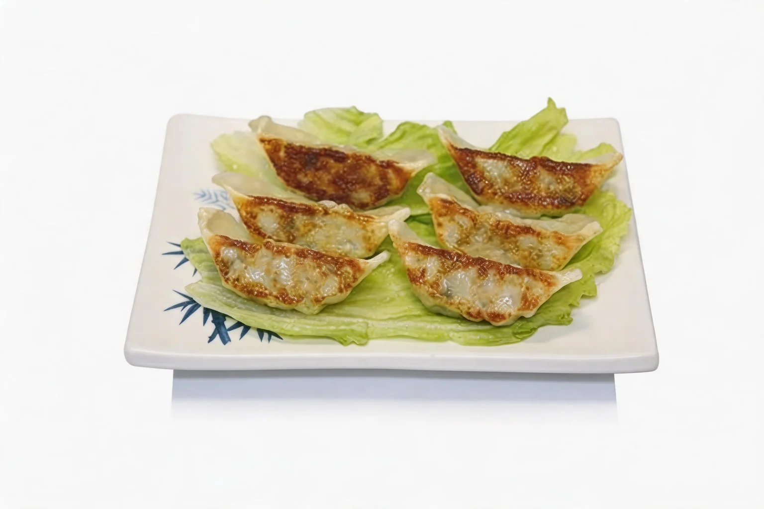 Six gyoza grillés sur un lit de salade, dans une assiette blanche à motif de bambou