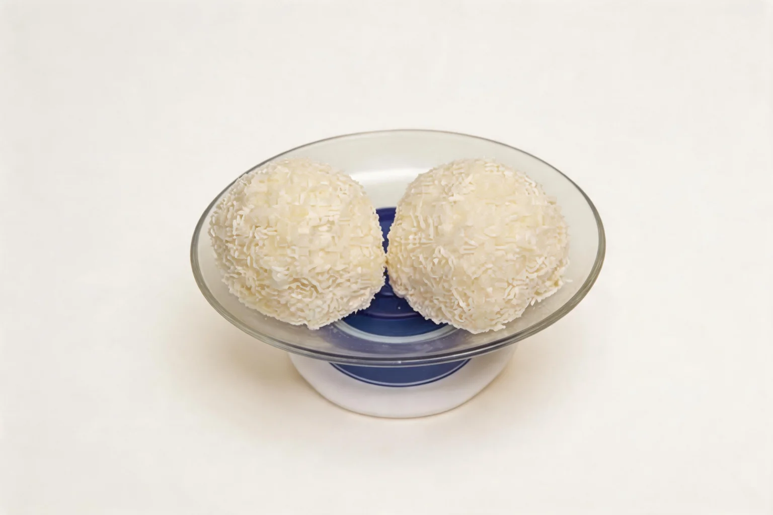 Deux boules enrobées de noix de coco râpée, servies dans une coupelle en verre bleu